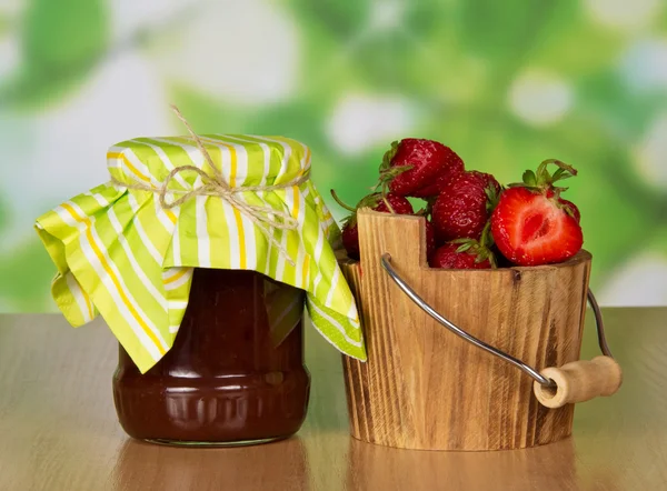 Bank with jam and a bucket with strawberry, on a table — Stock Photo, Image