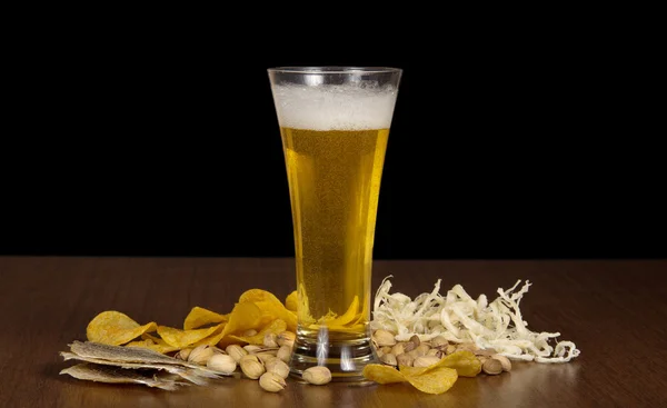Kieliszek spienionym piwem z pęcherzyków, chipsy, słone ryby, suszone kalmary i pistacji na stół — Zdjęcie stockowe