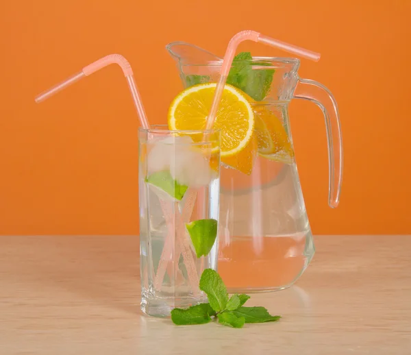 Jarro com bebida, um copo com palha e uma parte de laranja, em uma mesa — Fotografia de Stock