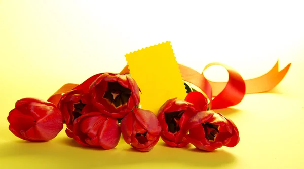 Het boeket van tulpen versierd met een tape en een lege kaart voor de tekst op een gele achtergrond — Stockfoto