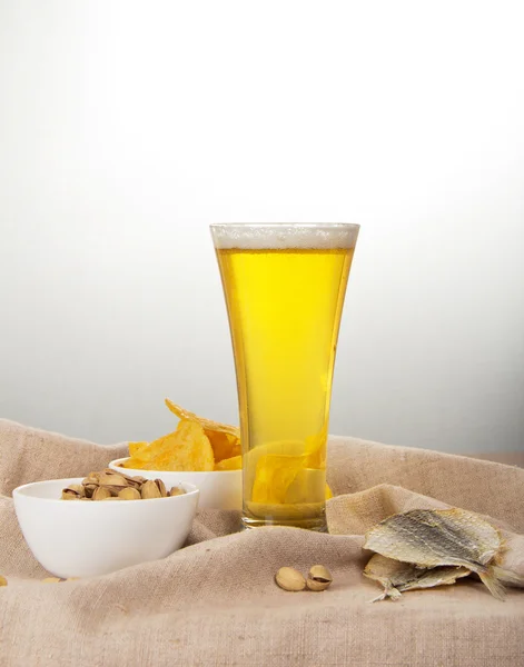 Sackcloth, glass of beer, pistachio, salty fish and fried potatoes — Stock Photo, Image