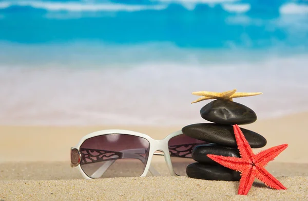 Sonnenbrille, Seesterne und Kieselsteine auf Sand — Stockfoto