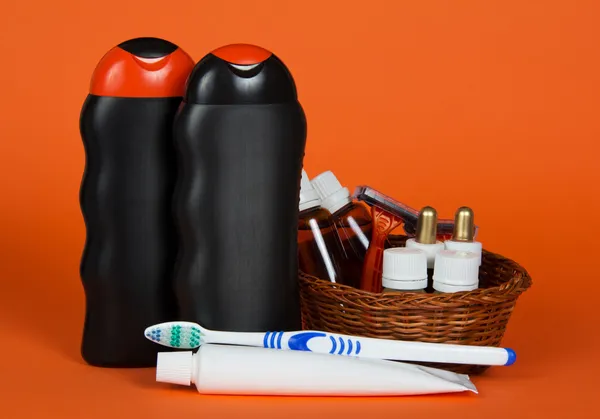 Шампунь, гель, косметика в корзине, зубная щетка и паста, на оранжевом фоне — стоковое фото