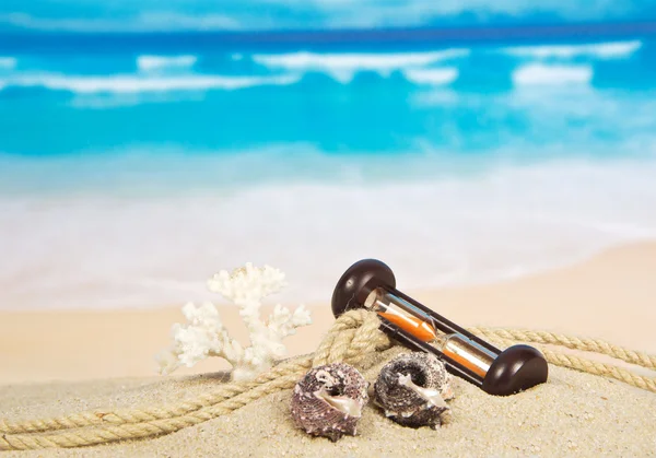 Sea cockleshells, hourglasses and a rope on sand — Stock Photo, Image