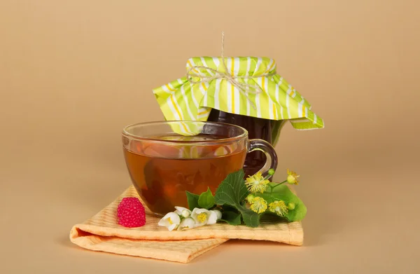 Raspberry jam, tea, flowers, napkin on a beige background — Stock Photo, Image