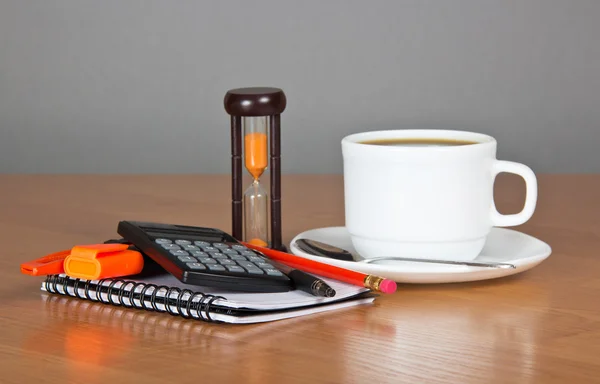 Lege pagina's notities, cutter, pen, markering een potlood de calculator, kopje koffie, schotel, lepel en hourglasses — Stockfoto