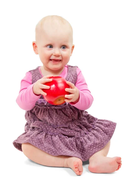 Süßes kleines Mädchen in violettem Kleid sitzt mit einem Apfel in der Hand. isoliert auf weiß — Stockfoto