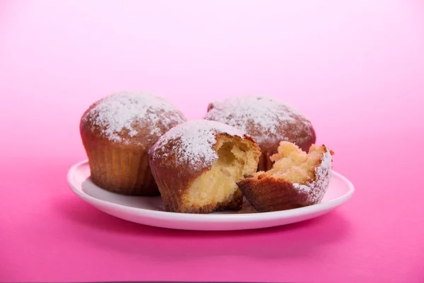 Cupcake on a dish, strewed with icing sugar, on a pink background — Stock Photo, Image