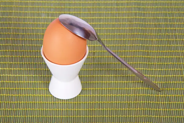 Egg in a support and a teaspoon on a green background — Stock Photo, Image