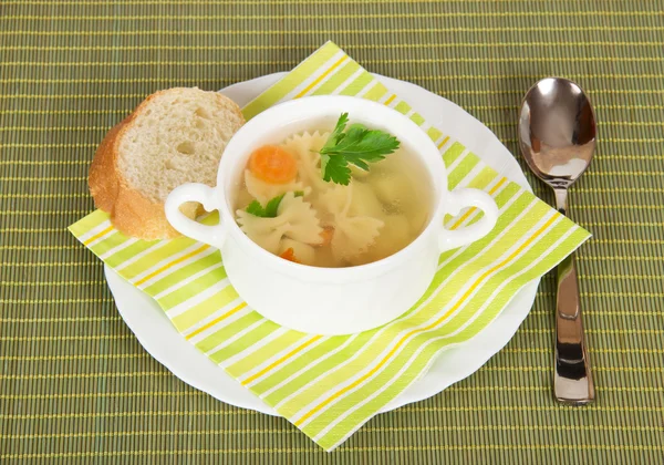 Schüssel mit Suppe, Brot, einem Teller, einem Löffel und einer Serviette auf einem grünen Bambustuch — Stockfoto