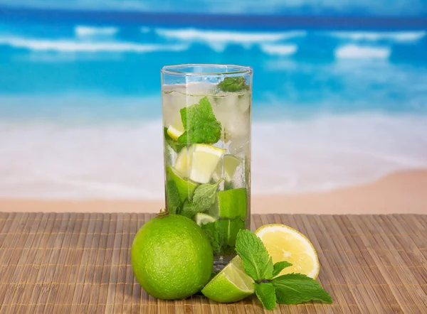 Glass med mojito, saftig lime og et peppermynteblad på en bambusduk mot havet – stockfoto