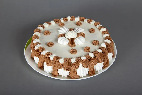 Bir tabak üzerinde gri bir arka plan üzerine krema ile süslü pasta — Stok fotoğraf