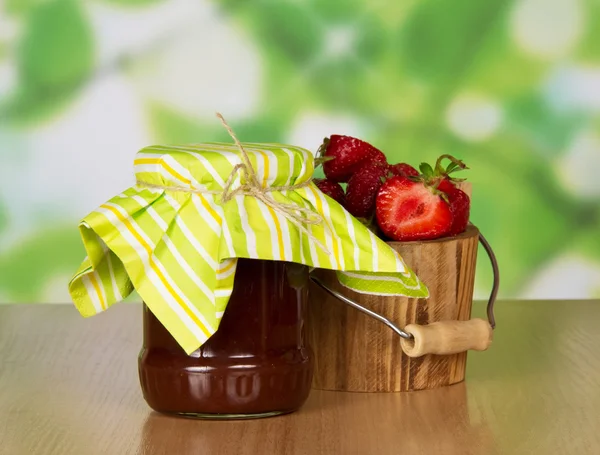 Bank with jam and a bucket with strawberry, on a table — Stock Photo, Image