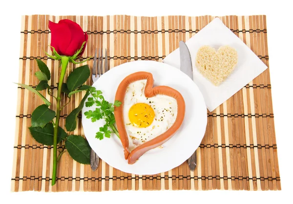 Sausage in the form of heart on a white plate, scrambled eggs and bread, red rose isolated on white — Stock Photo, Image