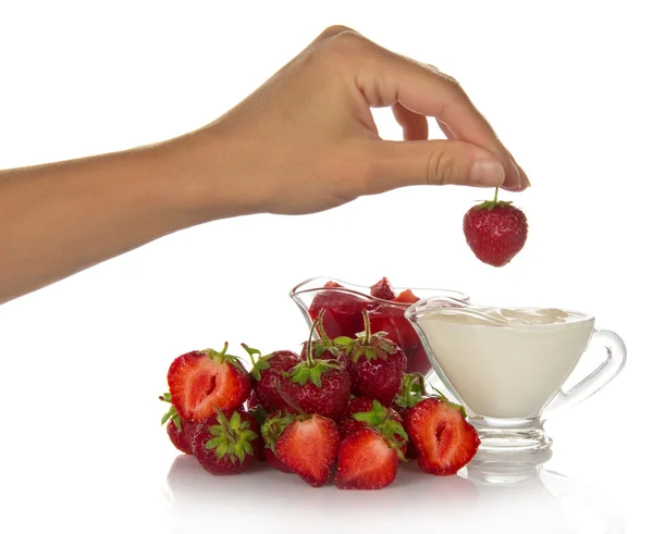 The cup with cream, a female hand holds strawberry berry by a tail, isolated on white — Stock Photo, Image