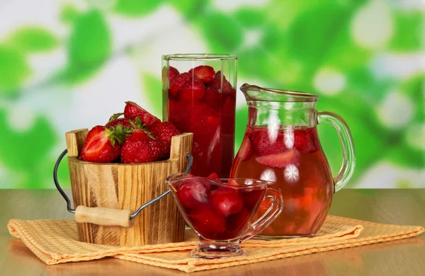 Jug with drink, strawberry in a bucket and in a glass, and berries in a cup, napkins on a table — Stock Photo, Image