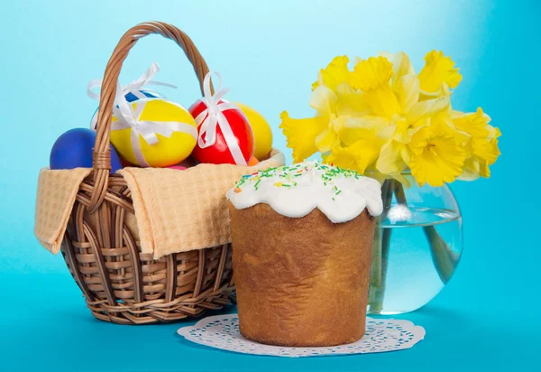 Eggs in a basket with a napkin, an Easter cake and a vase with narcissuses, on the blue — Stock Photo, Image