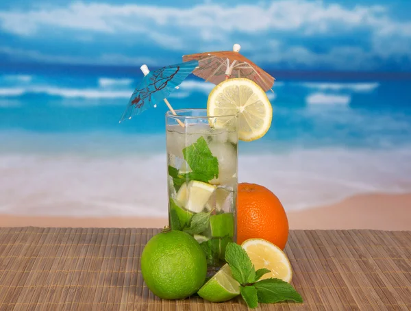 Mojito with umbrellas, orange, a juicy lime, a lemon on a bamboo cloth against the sea — Stock Photo, Image