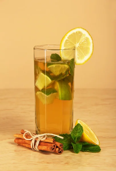 Le verre avec boisson est décoré d'une tranche de citron, d'un bâton de cannelle et de menthe sur une table. — Photo