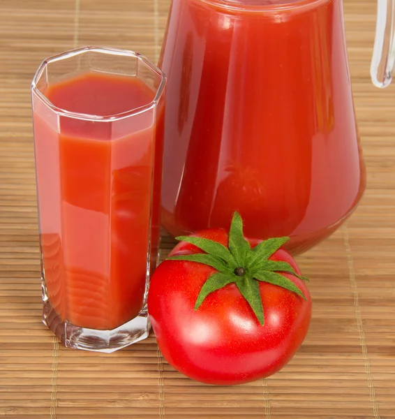 Krug und Glas mit Saft, Tomate gegen Bambustuch — Stockfoto