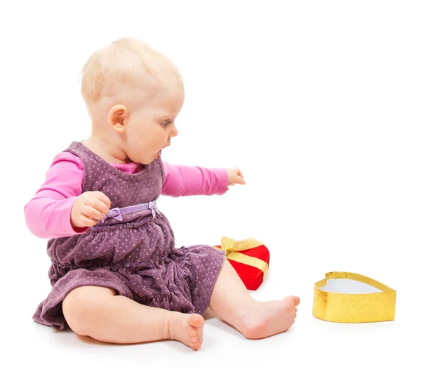 Das entzückte kleine Mädchen in violettem Kleid mit Rüschen sitzt auch goldene Schachtel in Herzform. isoliert auf weiß — Stockfoto