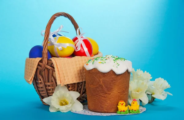 Œufs dans un panier, gâteau de Pâques, poulets de massepain et un bouquet de narcisses blanches, sur le bleu — Photo