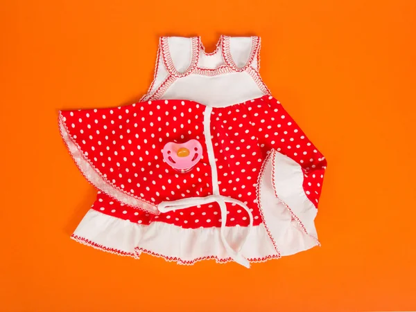 Children's dress, kerchief and pacifier, on an orange background — Stock Photo, Image