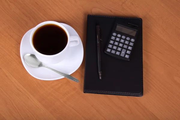 Blocco note, la maniglia la calcolatrice e una tazza di caffè su un tavolo — Foto Stock