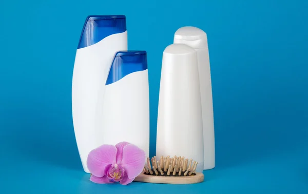 El juego de los cosméticos para el cuidado del cuerpo, la flor y el cepillo de pelo de madera sobre el fondo azul —  Fotos de Stock