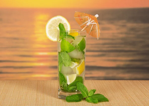 Cold drink with a lemon slice, spearmint, on a bamboo cloth against the sunset — Stock Photo, Image