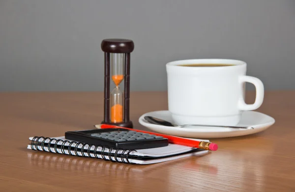 Tomma sidor för anteckningar en penna kalkylatorn, kopp kaffe, tefat, sked och timglas — Stockfoto
