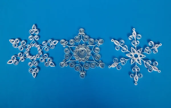 Tres copos de nieve de Navidad de papel, hechos a sí mismos. Sobre fondo azul — Foto de Stock