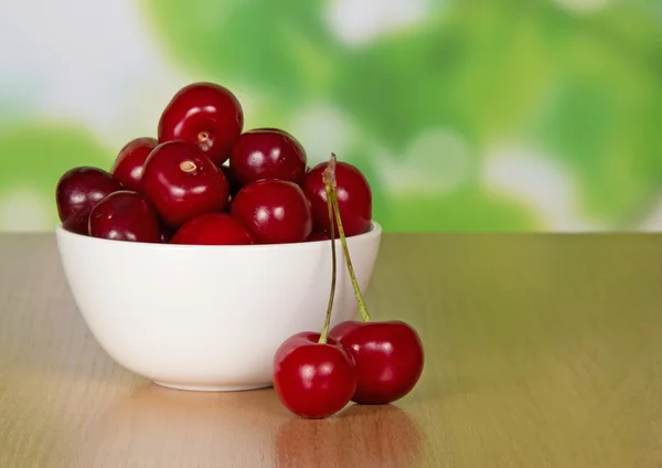 Sweet cherries in a ceramic cup and two berries on a table — Stock Photo, Image