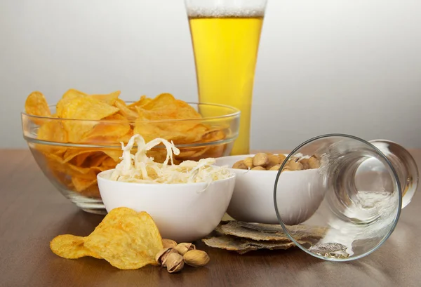 Los diversos aperitivos, vaso lleno de cerveza y vaso vacío sobre un fondo gris — Foto de Stock