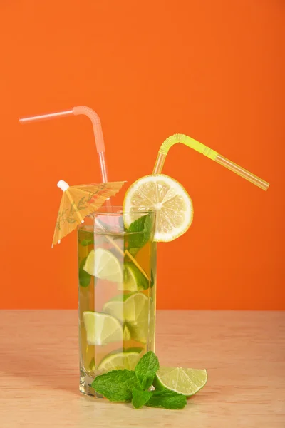 Boire avec une paille, est décoré avec une tranche d'un citron et un parapluie, un citron vert mûr et menthe, sur une table — Photo