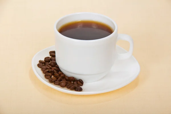 Weiße Tasse Kaffee mit Körnern auf einer Untertasse — Stockfoto