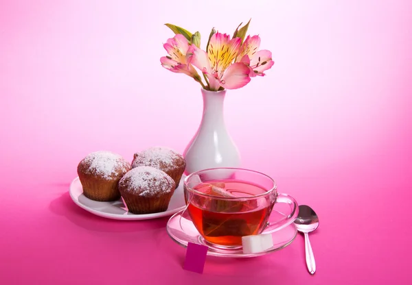 Cup of tea and sugar on a saucer, a teaspoon, an alstroemeria in a vase, on a pink background — Stock Photo, Image