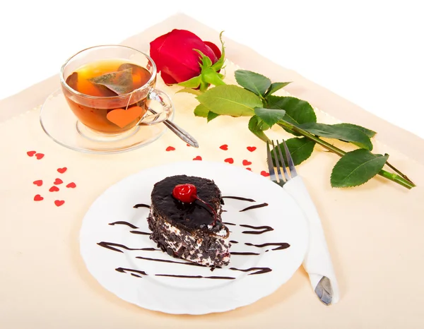 Шоколадный торт, горячий чай и красная роза на ткани, украшенной сердцами — стоковое фото