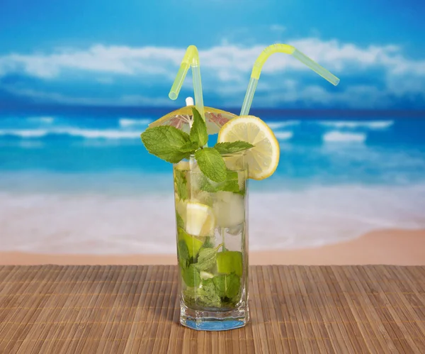 Mojito with cocktail straws and a lemon slice, on a bamboo cloth against the sea — Stock Photo, Image