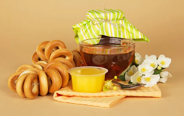 Cup of tea, honey, jam bank, a linking of bagels, flowers and a napkin on the beige — Stock Photo, Image