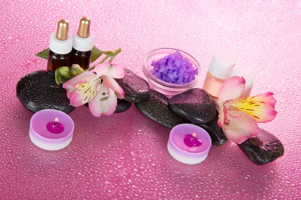 Aceite aromático, sal, velas, piedras, flores, en gotas de agua, sobre fondo rosa —  Fotos de Stock