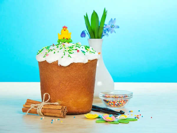 Påsk kaka, söta smycken, kryddor, vas med blommor på ett bord, på en blå bakgrund — Stockfoto