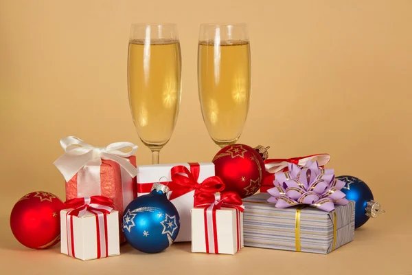 Due bicchieri di vino con champagne, affascinanti scatole regalo e giocattoli di Natale su sfondo beige — Foto Stock