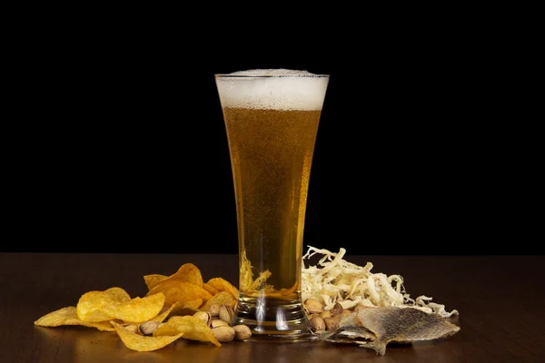 Verre de bière mousseuse avec bulles, croustilles, poisson salé, calmar séché et les pistaches sur la table — Photo