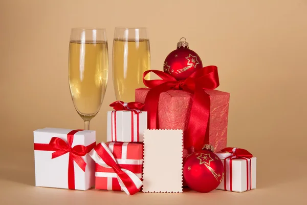 Weingläser mit Champagner, Weihnachtsgeschenke und Spielzeug und leere Karte für Botschaften auf beigem Hintergrund — Stockfoto