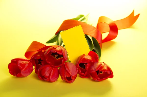 Букет тюльпанов украшен лентой и пустой карточкой для текста на желтом фоне — стоковое фото