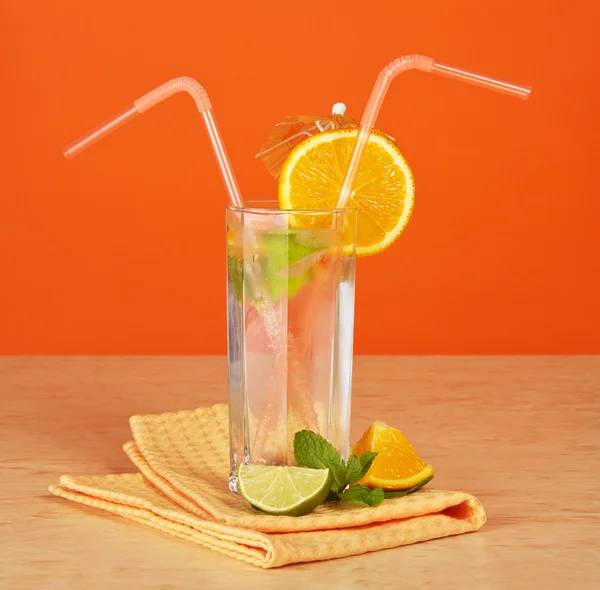 O copo de bebida com uma palha, decora-se com um guarda-chuva e um segmento cor-de-laranja, uns cítricos e um guardanapo em uma mesa — Fotografia de Stock
