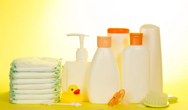 Objets de soins pour bébés. Olive, shampooing, couches sur fond jaune — Photo