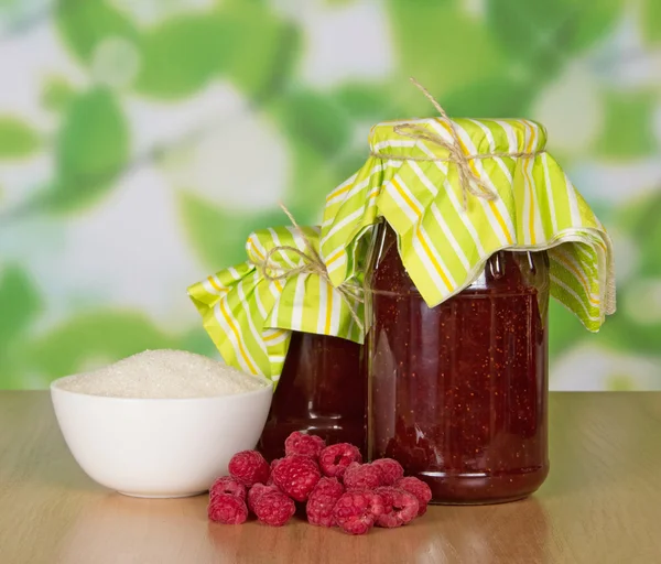 Jars of jam, a cup of sugar and handful of berries on a table — Stock Photo, Image