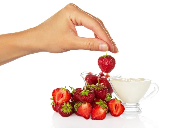 La taza con la crema, la mano femenina sujeta la baya de fresa por la cola —  Fotos de Stock